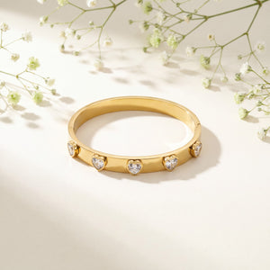 Gold bracelet with heart-shaped gemstones on a light background with delicate flowers.