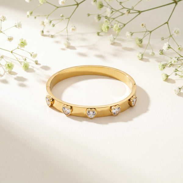 Gold bracelet with heart-shaped gemstones on a light background with delicate flowers.
