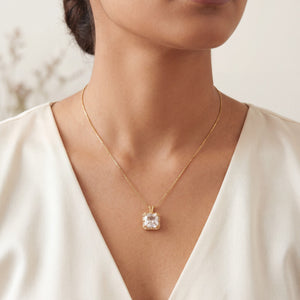 Gold necklace with a diamond pendant worn by a person in a white dress.