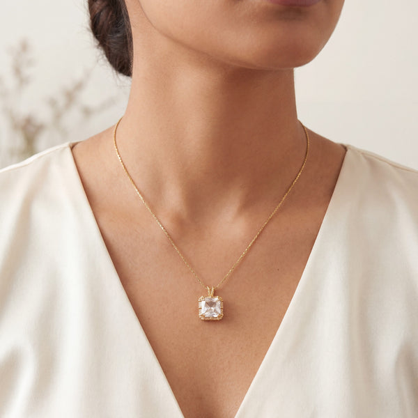 Gold necklace with a diamond pendant worn by a person in a white dress.