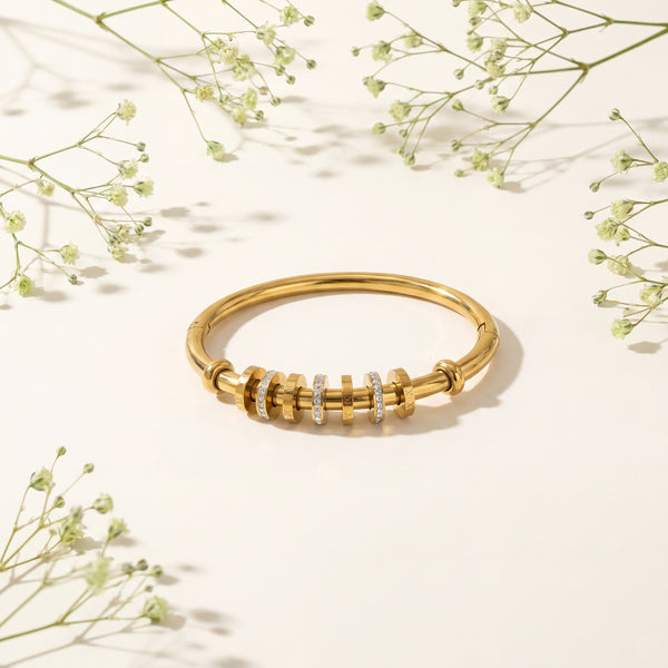 Gold bracelet with small diamonds on a light background with delicate greenery